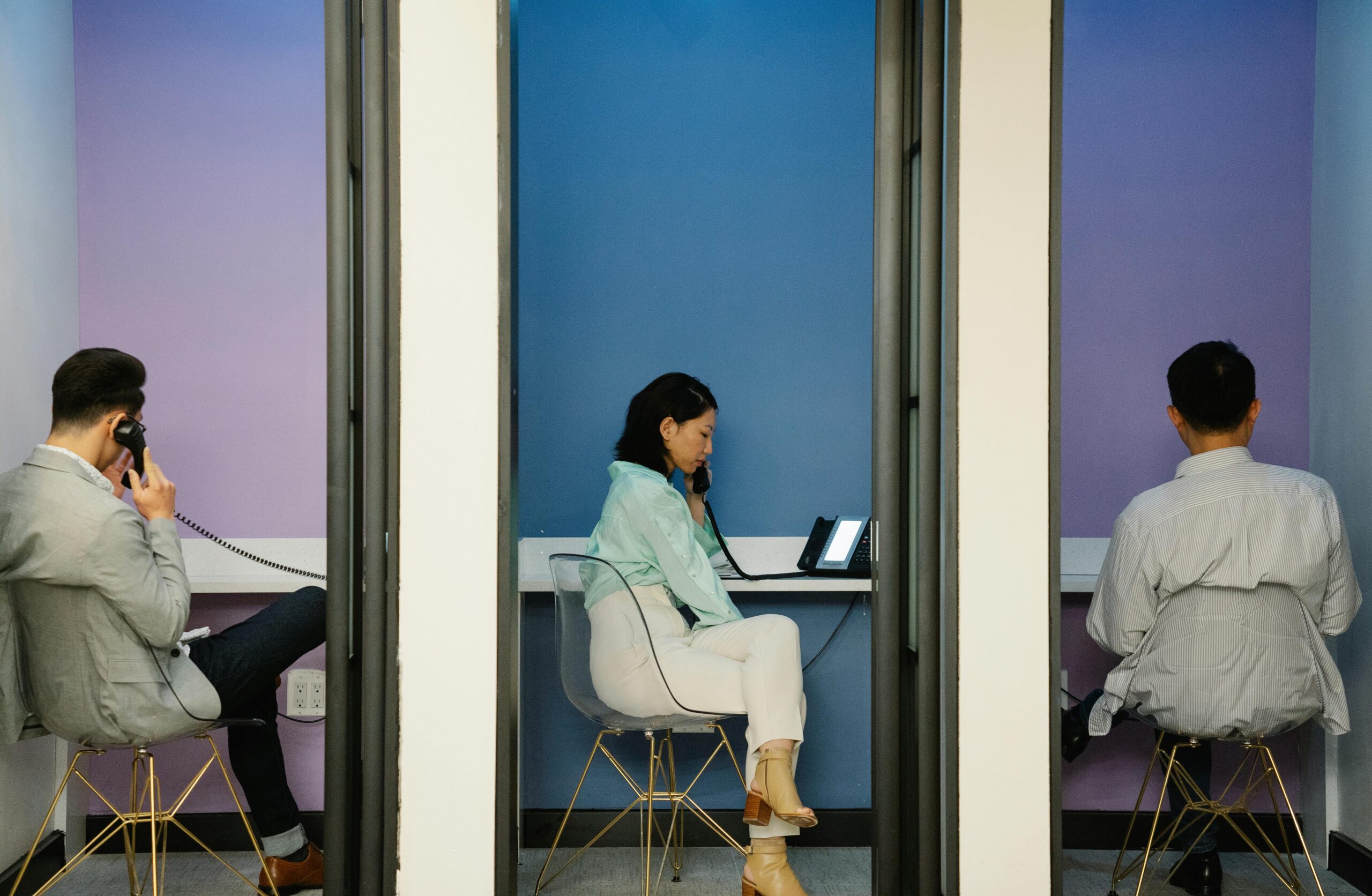Three business professionals making phone calls in isolated booths, emphasizing privacy.
