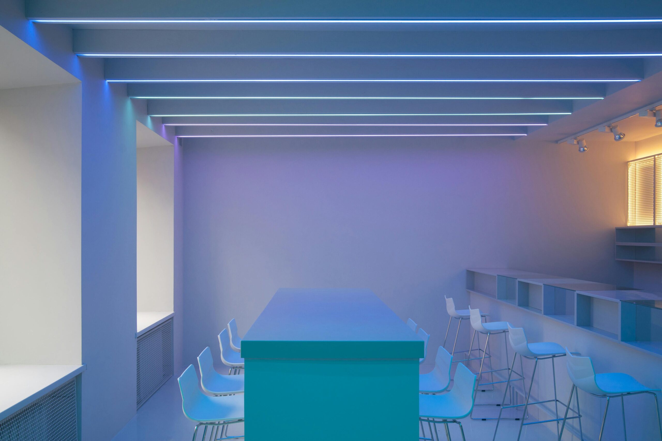 Sleek minimalist interior with blue neon lights and white bar chairs.